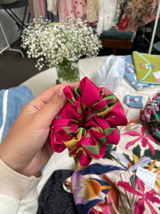 Hårstrikk i sateng med fuksia og grønt mønster, holdt i en hånd